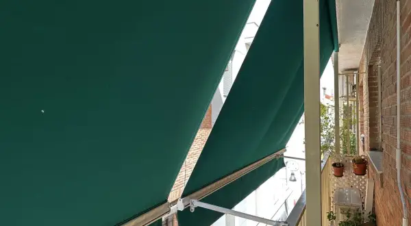 La lona verde protege del sol en un balcón con ladrillos.