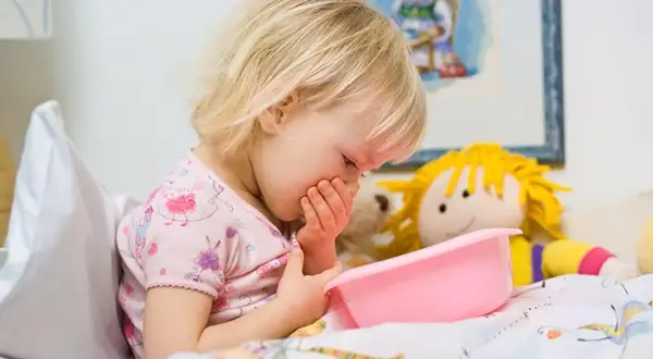 Niña rubia con vómito, posiblemente por rotavirus en niños. Sostiene un recipiente rosa.