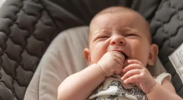 Un bebé de 3 meses intenta incorporarse, con su mano en la boca, en una hamaca acolchada.