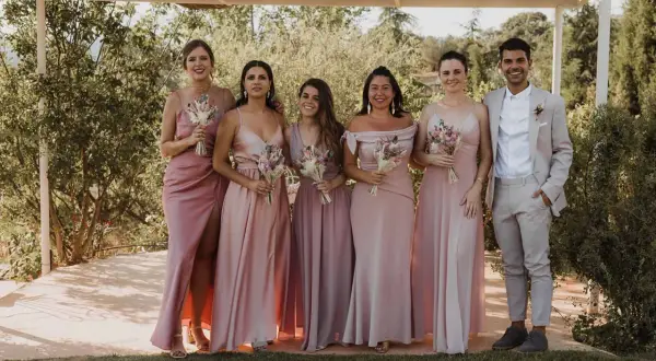 Seis damas de honor con vestidos rosas y un novio con traje claro. Un ejemplo perfecto de como vestirse para una boda de dia.