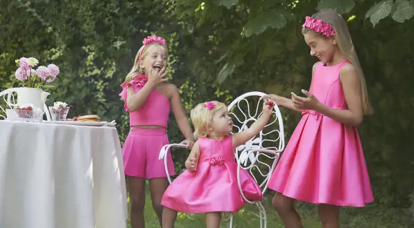 Niñas con vestidos fucsia, una con un fajín para vestido niña, disfrutan de un té en el jardín.