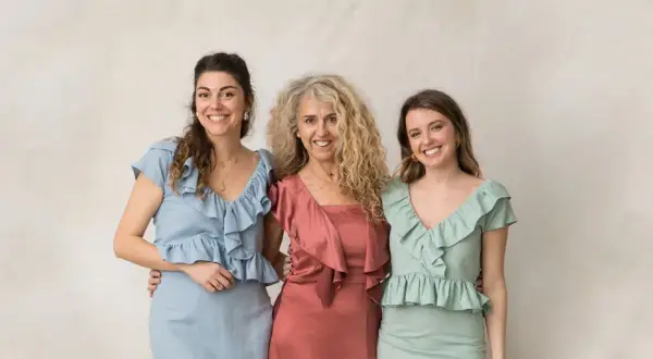 Tres mujeres sonríen, vestidas con trajes elegantes. Ideas para como vestir para un bautizo en invierno.