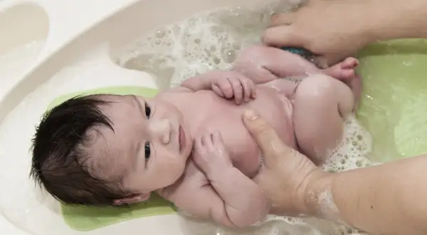 Un bebé sonriente disfruta de su primer baño. Aprende cuando bañar a un recién nacido con este tierno momento.