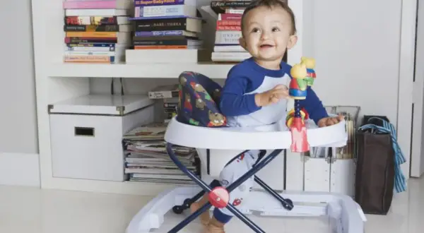 Bebé sonriente en andador, rodeado de libros. Posibles consecuencias del uso del andador en bebés.