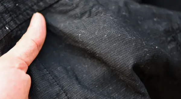 Dedos señalan motas negras en ropa oscura, resultado de la lavadora.