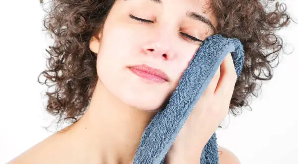 Mujer con rizos oscuros se seca la cara con toallas suaves y con buen olor, disfrutando de un momento de frescura.
