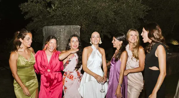 Seis mujeres posan sonrientes, luciendo vestidos elegantes, perfectos para saber como ir vestida a una boda de noche.