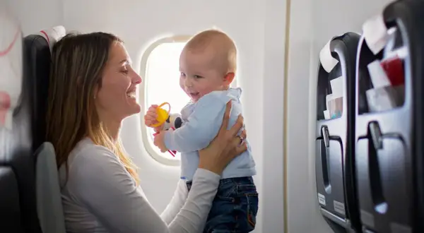 Madre sonríe a su bebé en un avión, jugando con un sonajero. Viajar con bebés puede ser una aventura alegre.