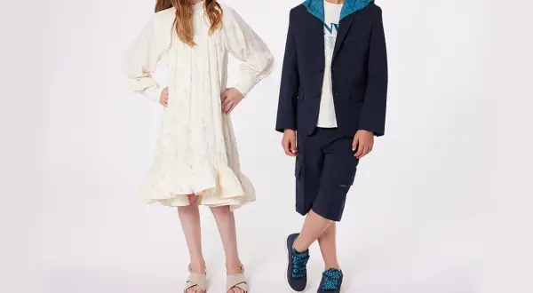 Niño y niña posan con atuendos elegantes. Ideas para como vestir a un niño de 14 años para una boda: traje azul marino con capota y bermudas.