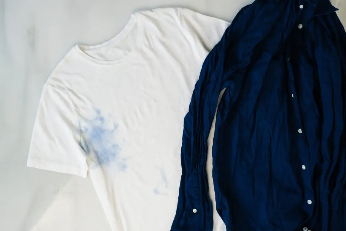 Camiseta blanca con manchas azules y camisa azul marino. Aprende como quitar el desteñido de la ropa de color.