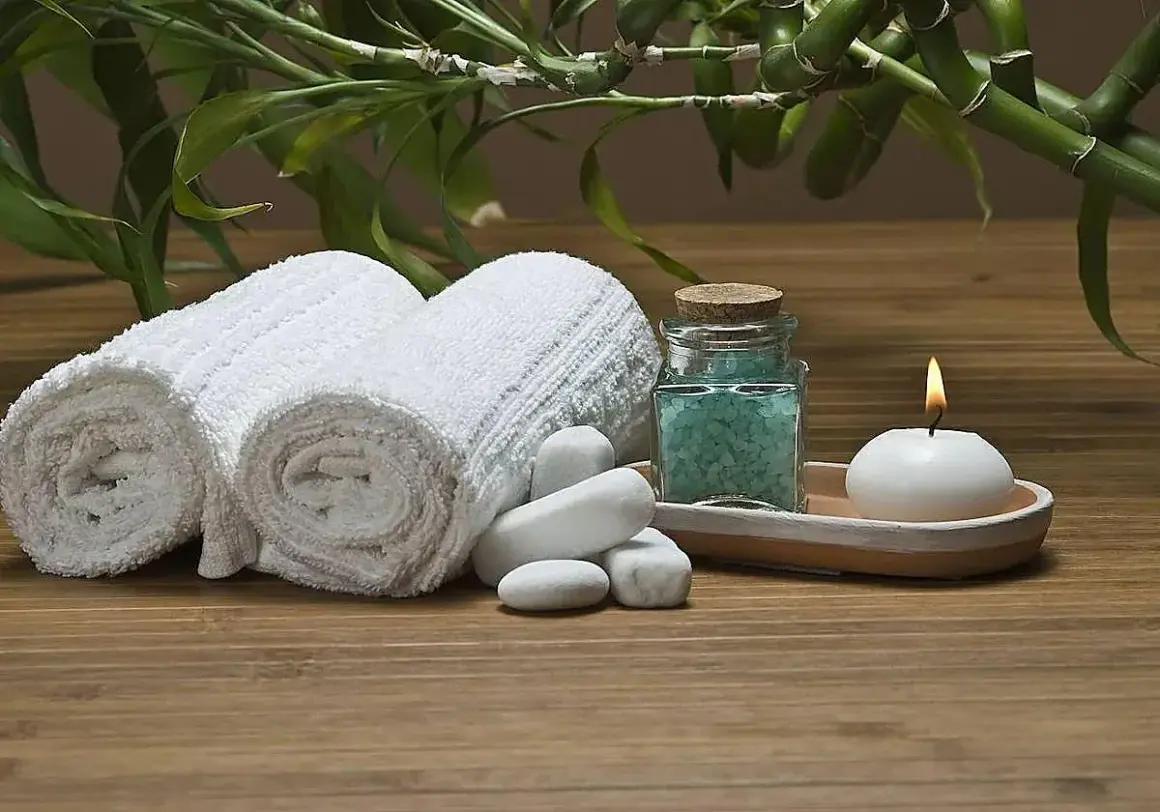 Toallas blancas enrolladas, sales de baño azules, vela encendida y bambú, ideal para recuperar toallas ásperas y disfrutar de un momento de spa.