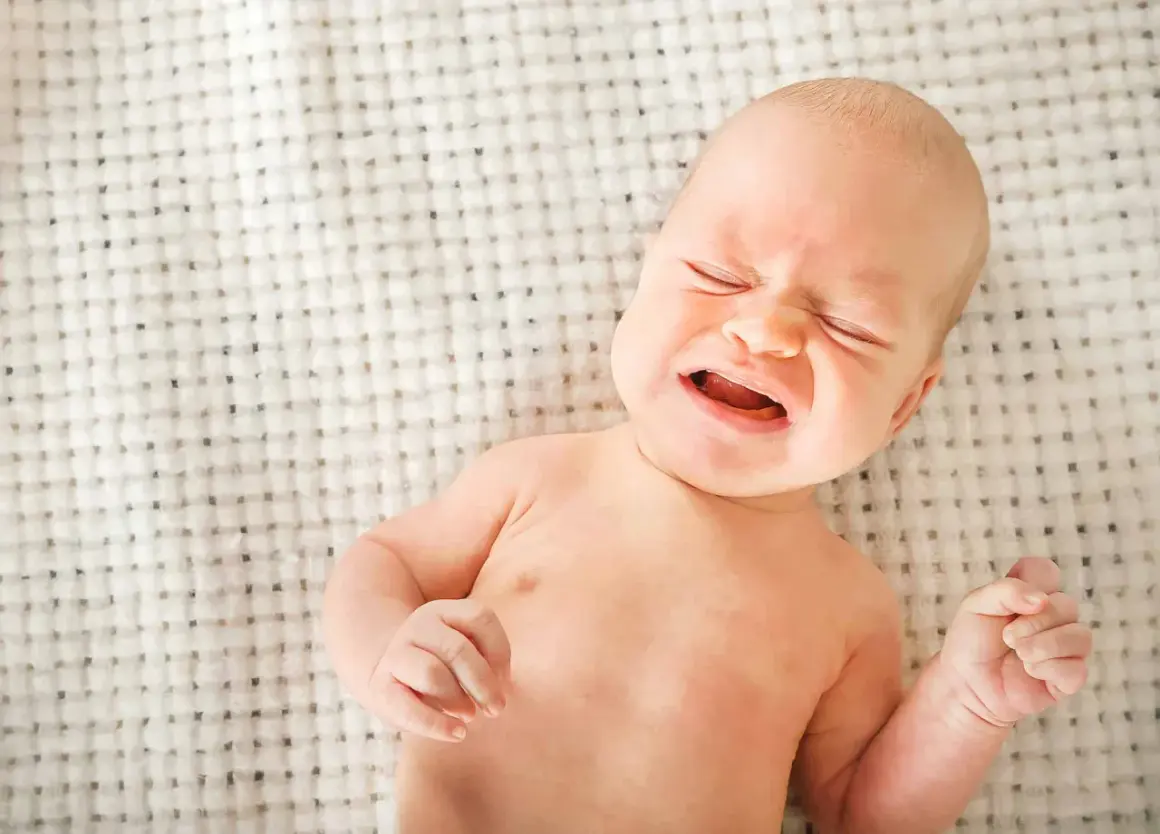 Bebé llorando, con ojos cerrados y boca abierta. Podría ser uno de los signos de deshidratación en bebés.