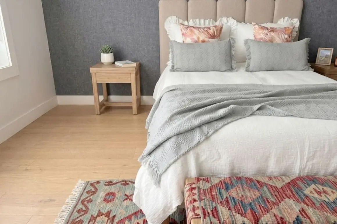 Cama acogedora con colcha de lino que da calor. Cojines grises y alfombra de estilo étnico.