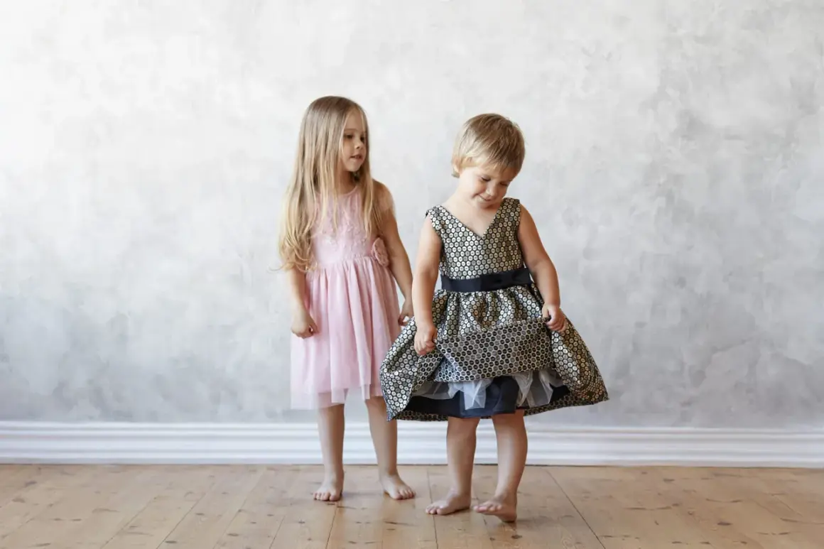 Dos niñas, una con un vestido rosa y otra con uno dorado y negro, muestran la ropa que llevan los niños en una boda.