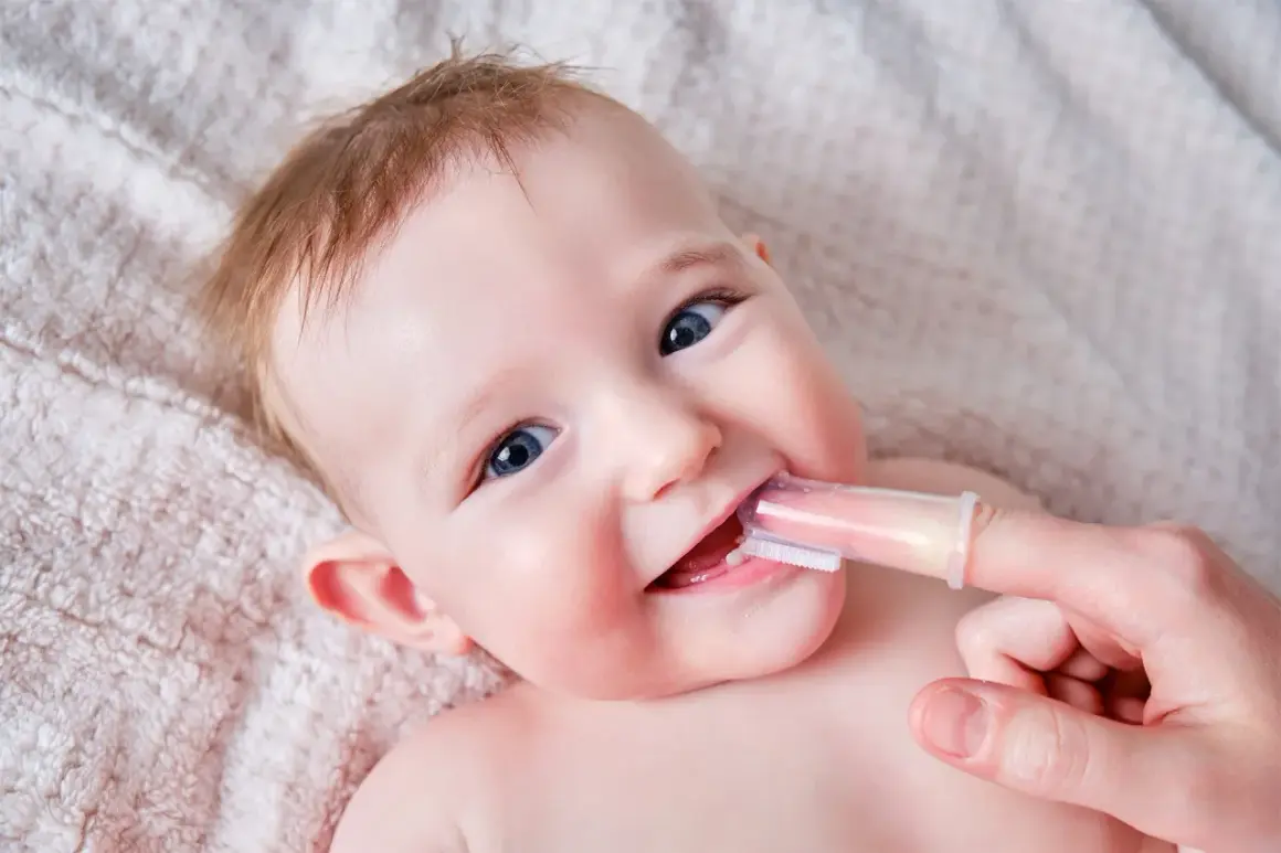 Bebé sonriente con sus primeros dientes siendo limpiados con un cepillo de dedo.