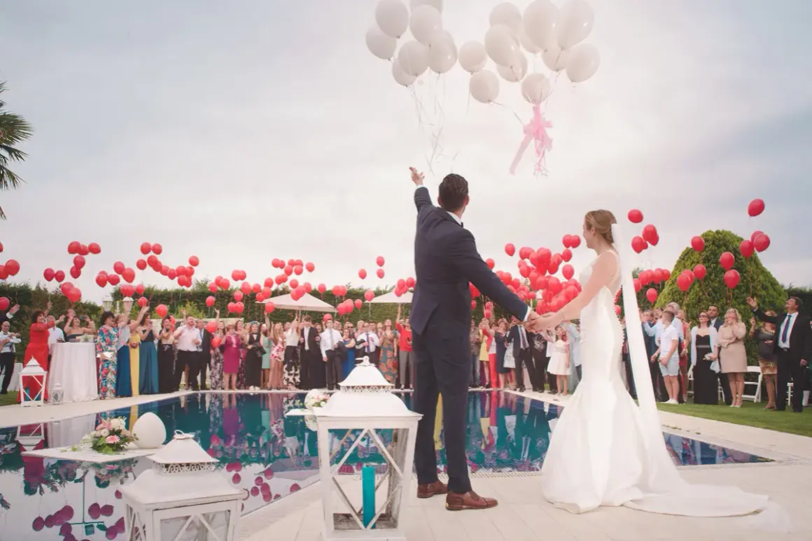 Novios liberando globos en una boda, rodeados de invitados y niños.