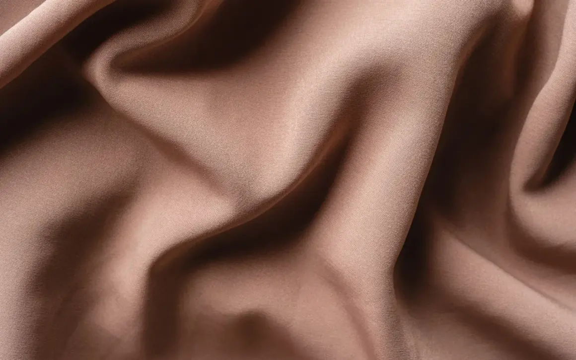 Textura de tela de satén color caramelo con pliegues suaves y sombras profundas. El satén se arruga, creando un efecto visual interesante.