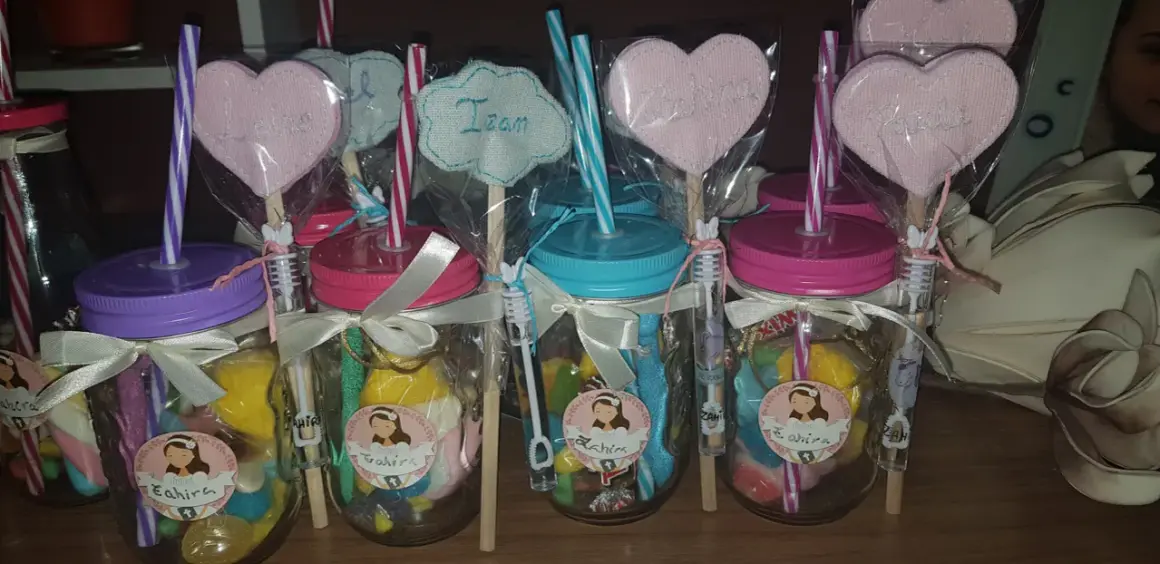 Frascos de comunión con dulces, pajitas y adornos de corazón con nombres.
