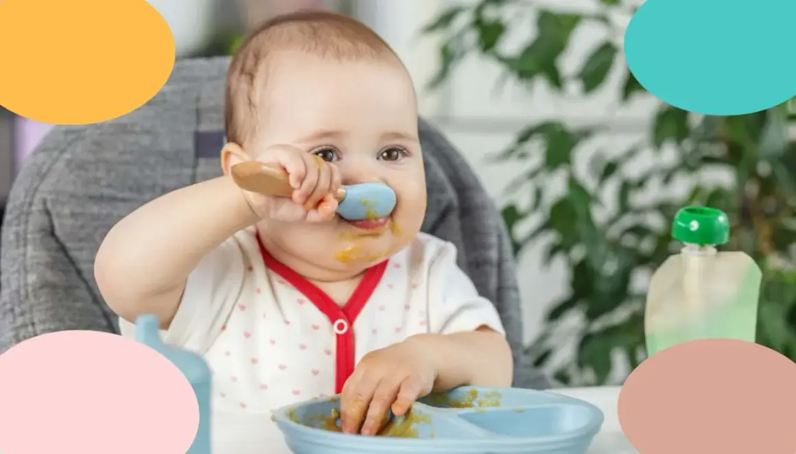 Un bebé de 12 meses, con la cara manchada de comida, intenta alimentarse solo con una cuchara azul.