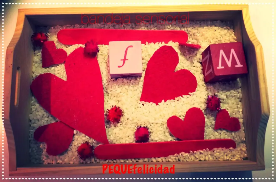 Bandeja sensorial de San Valentín para niños con corazones rojos, cubos con letras y arroz.