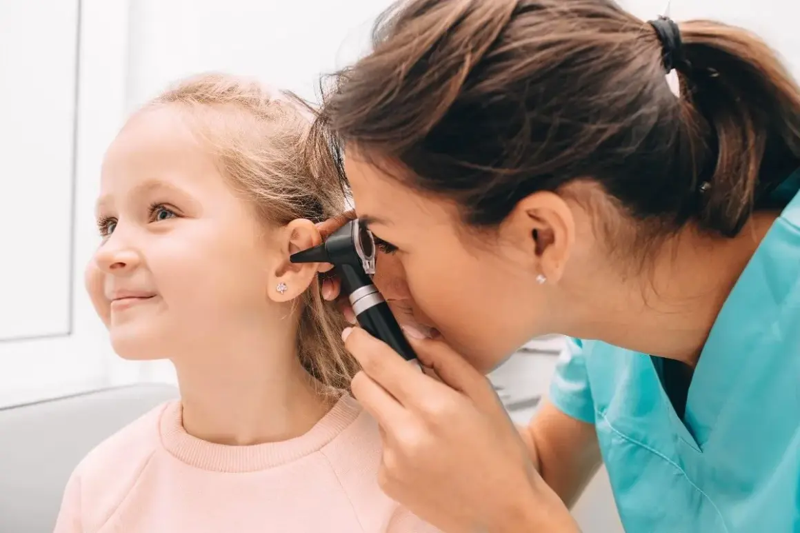 Médico examina el oído de una niña con otoscopio. Una revisión para descartar otitis en niños.