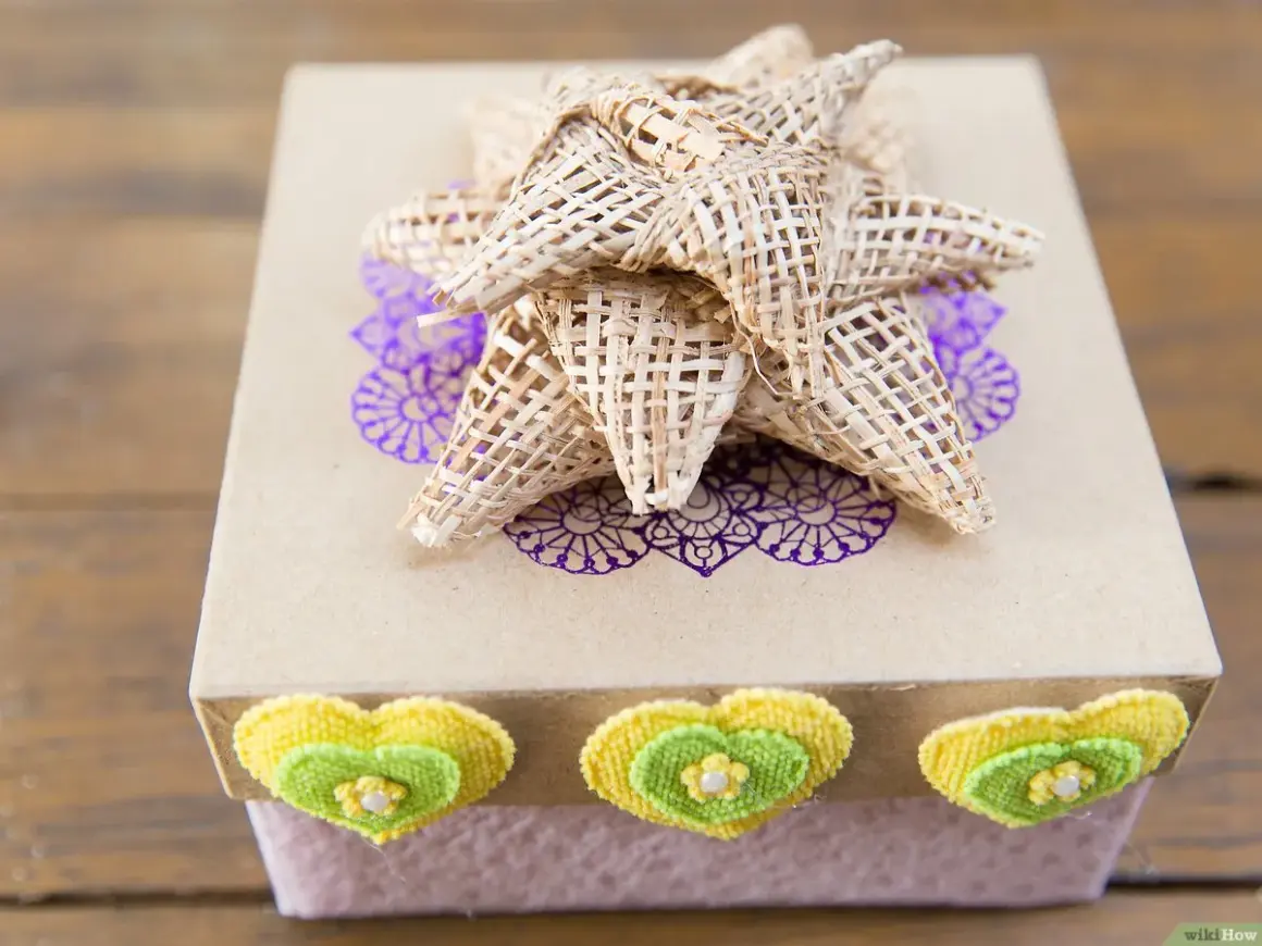 Caja de regalo decorada con un lazo grande de tela, corazones y un diseño floral.
