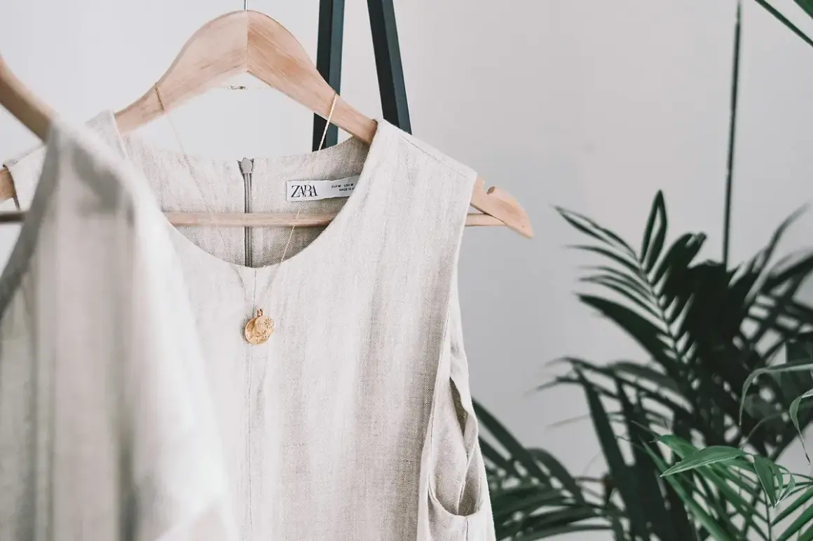 Vestido de lino beige colgado en percha, con collar dorado. Descubre trucos para que no se arrugue el lino y mantén tu ropa impecable.