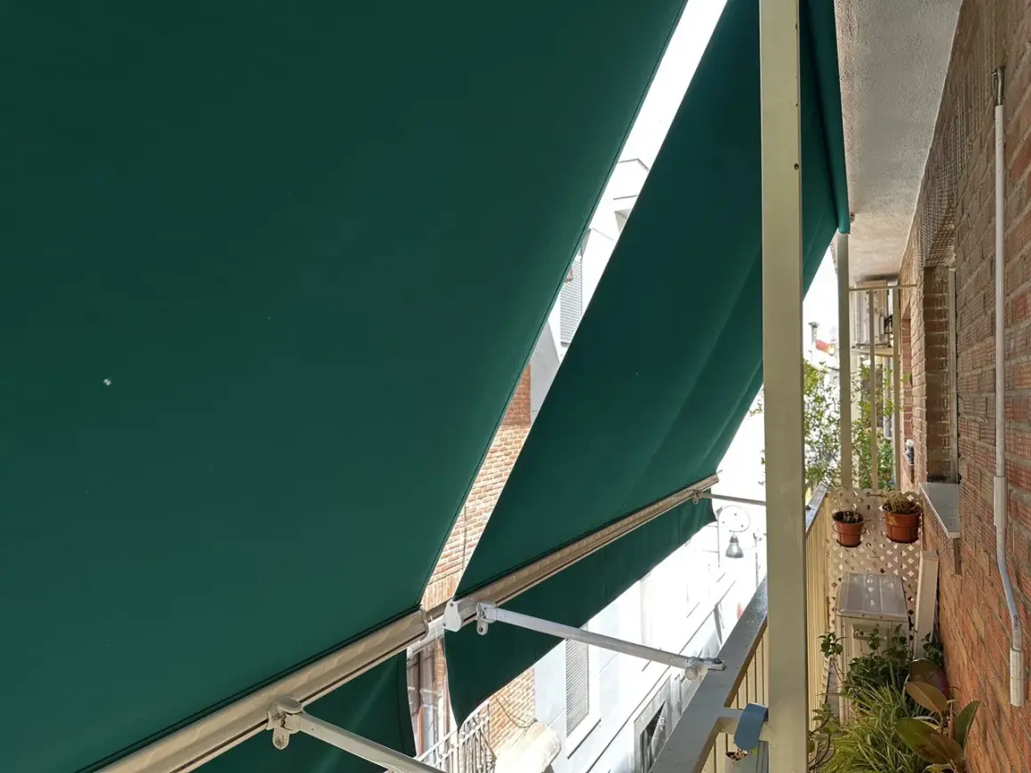 La lona verde protege del sol en un balcón con ladrillos.
