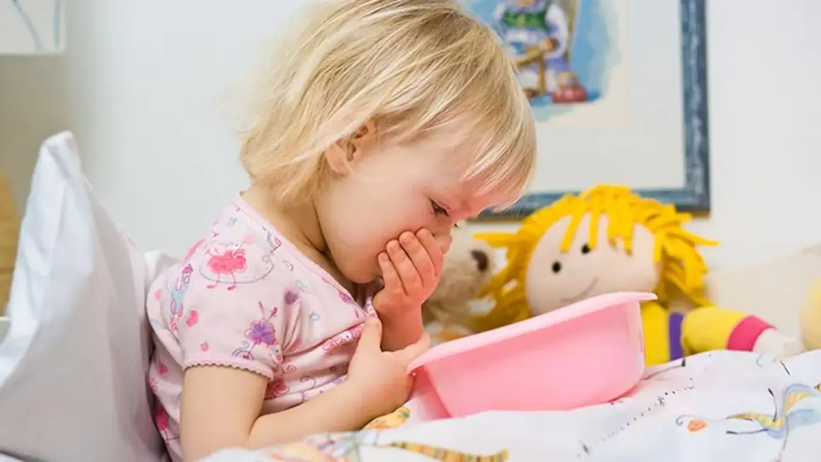 Niña rubia con vómito, posiblemente por rotavirus en niños. Sostiene un recipiente rosa.