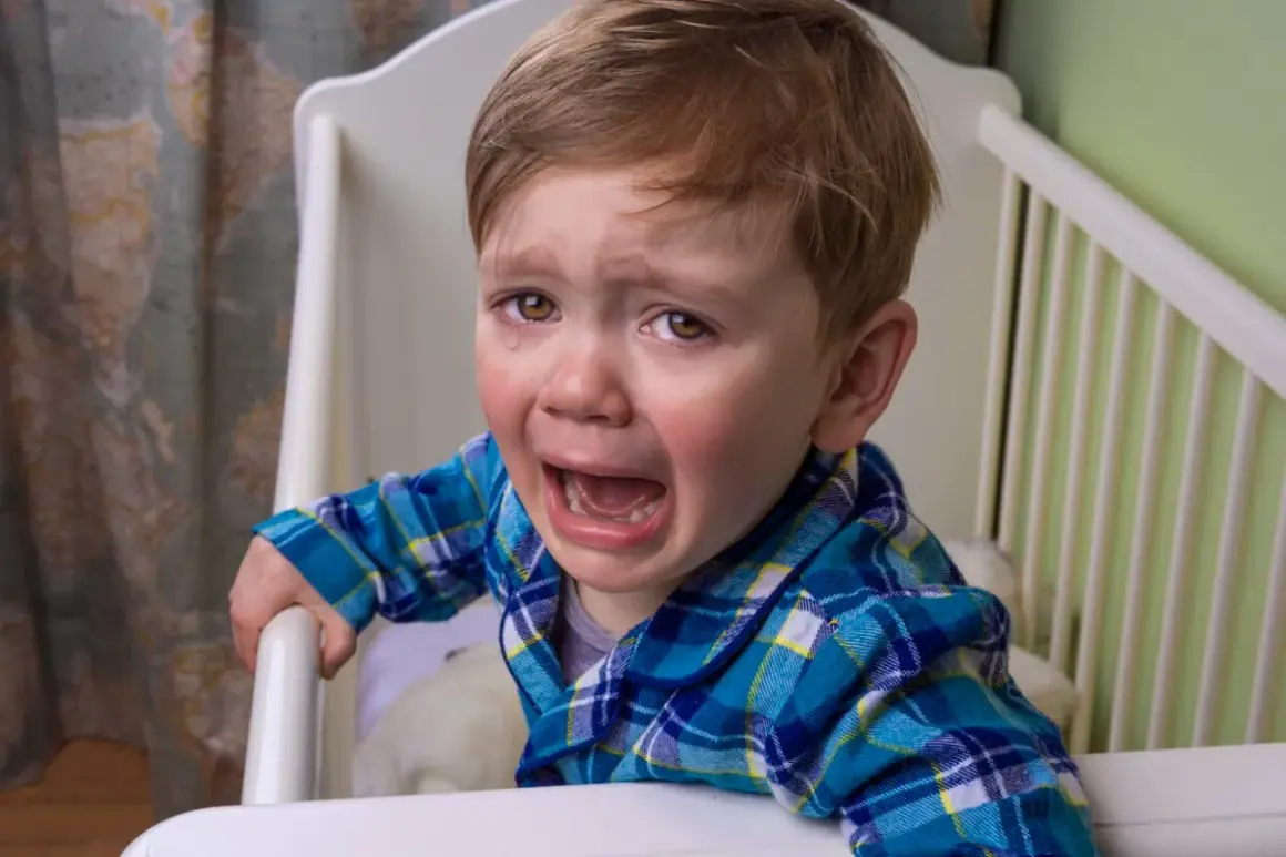 Un niño pequeño con pijama a cuadros azules llora desconsoladamente en su cuna. Mi bebé llora con mucha rabia, con lágrimas corriendo por sus mejillas.