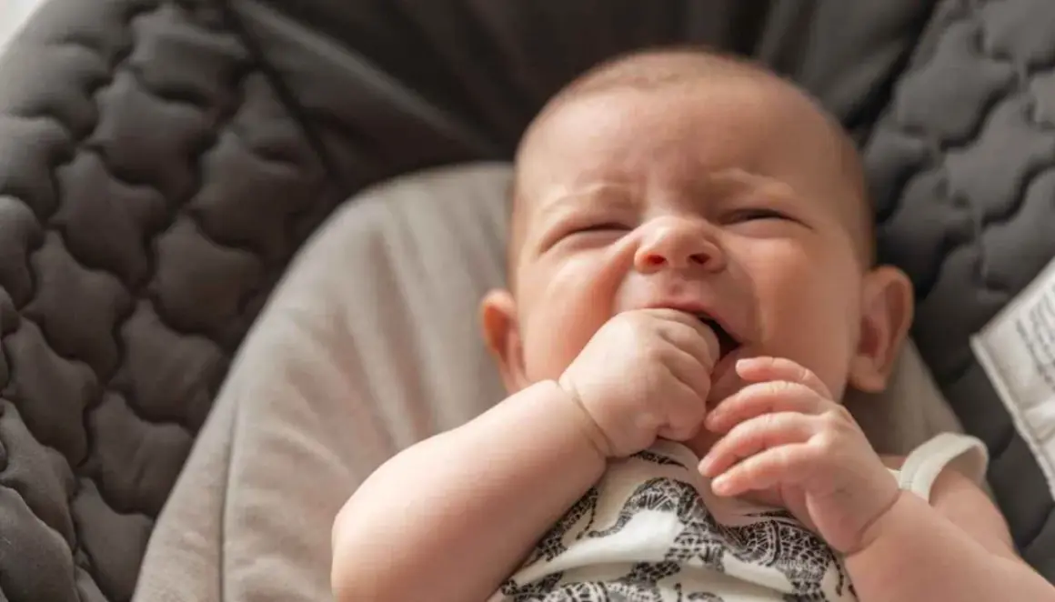 Un bebé de 3 meses intenta incorporarse, con su mano en la boca, en una hamaca acolchada.