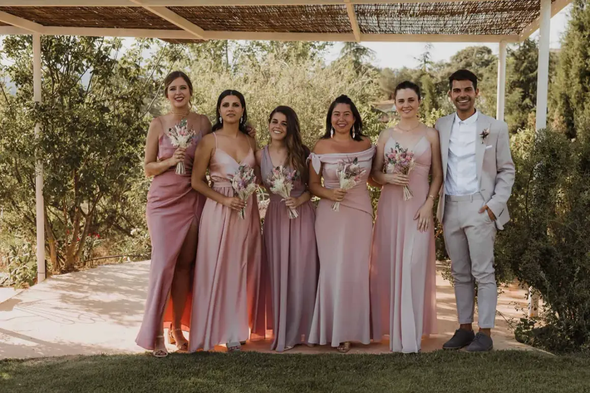 Seis damas de honor con vestidos rosas y un novio con traje claro. Un ejemplo perfecto de como vestirse para una boda de dia.
