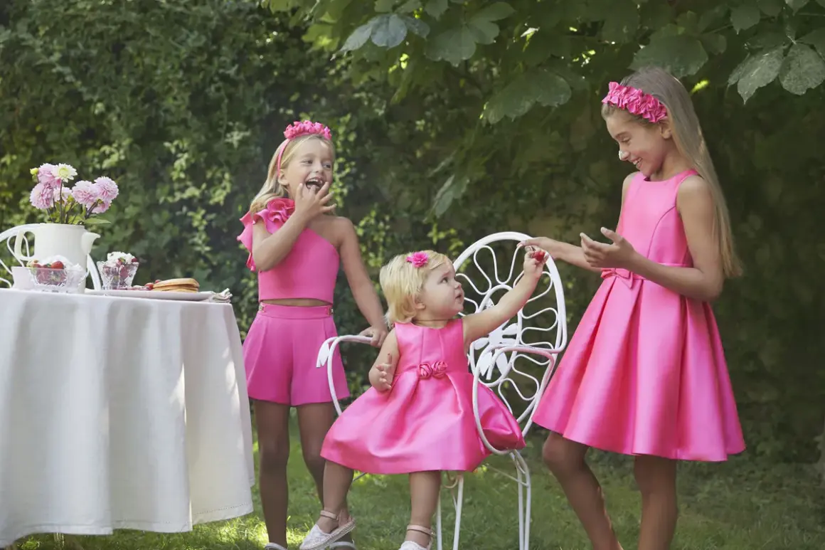 Niñas con vestidos fucsia, una con un fajín para vestido niña, disfrutan de un té en el jardín.