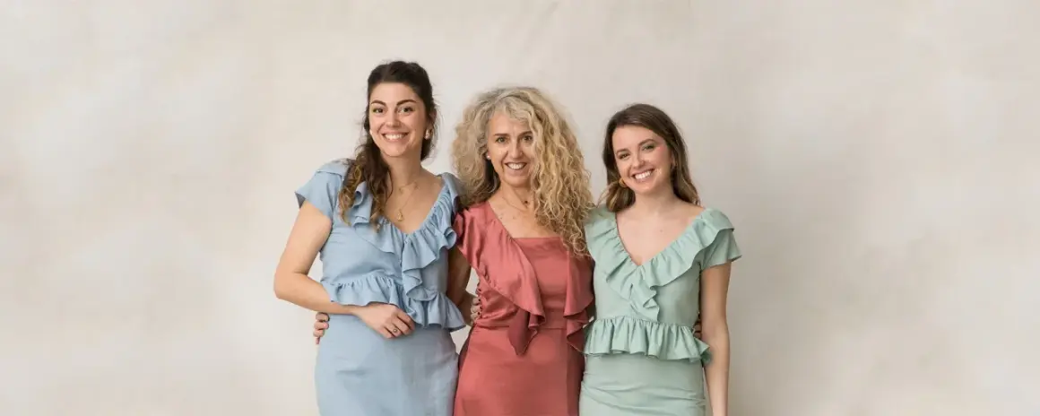 Tres mujeres sonríen, vestidas con trajes elegantes. Ideas para como vestir para un bautizo en invierno.