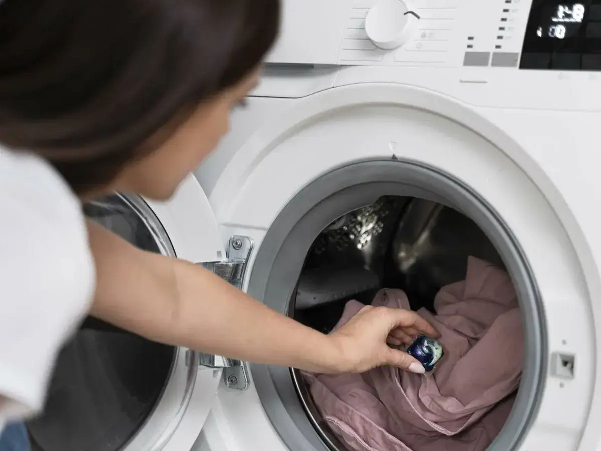 Mujer introduce una c&aacute;psula de detergente en la lavadora para un centrifugado suave de la ropa delicada.