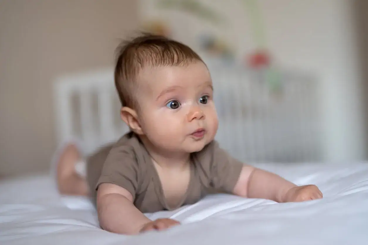 Un adorable bebe de 5 meses, con su carita curiosa, practica el gateo en una cama blanca.