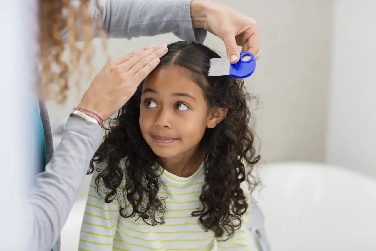 Una mano peina el cabello de una ni&ntilde;a con un peine azul, parte del tratamiento piojos ni&ntilde;os.
