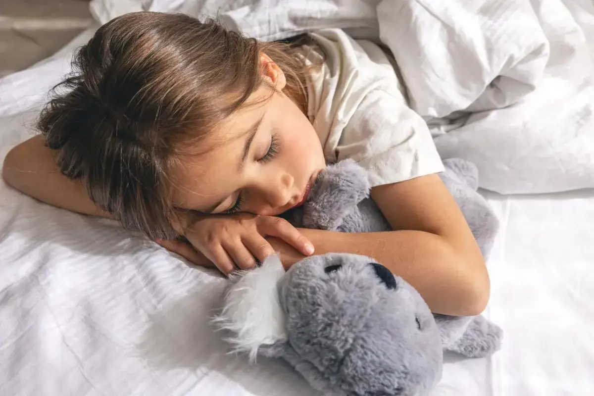 Niña duerme plácidamente abrazando a su peluche. Un sueño reparador es clave, como la melatonina para niños.