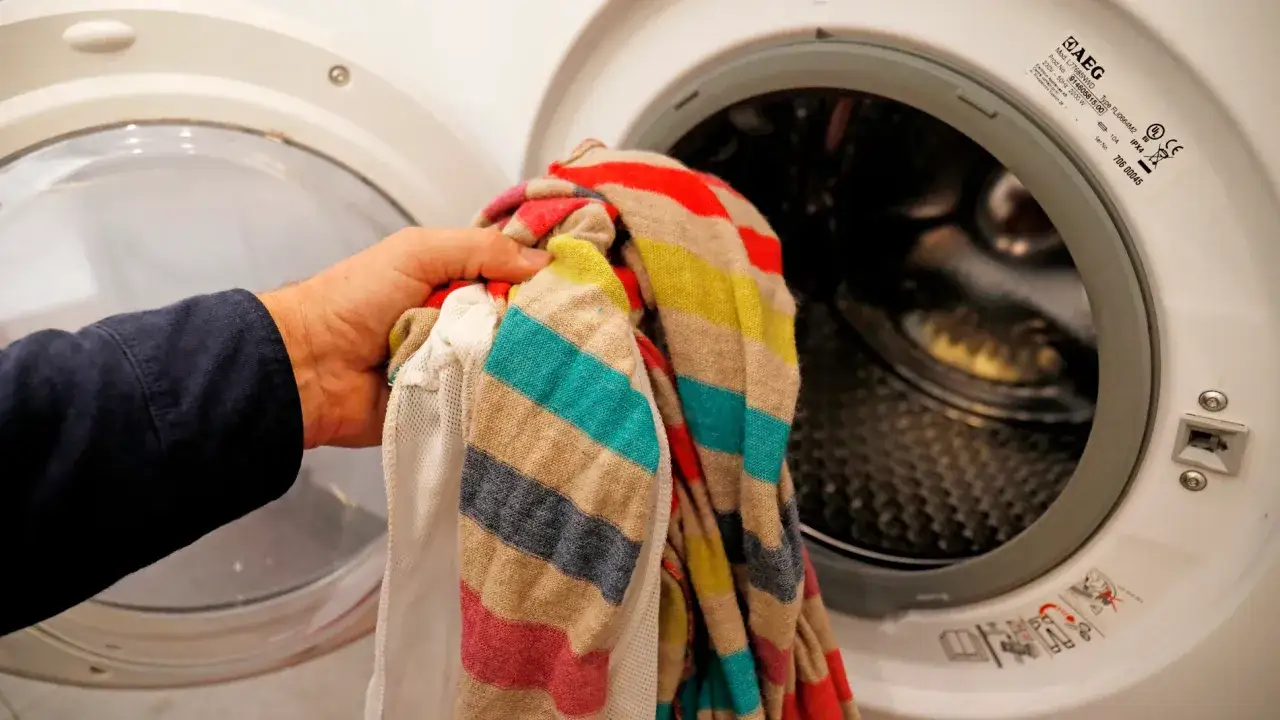 Mano introduce ropa a rayas en lavadora. Es malo poner la lavadora con poca ropa, desperdicia energ&iacute;a y agua.