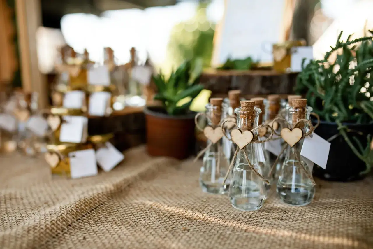 Peque&ntilde;as botellas de vidrio con corcho, decoradas con corazones de madera y etiquetas blancas, perfectas como detalles comuni&oacute;n.