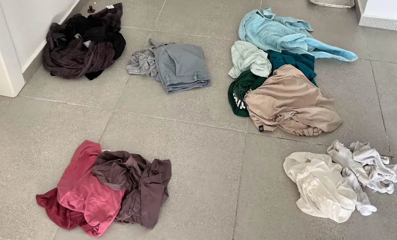 Ropa tirada en el suelo, incluyendo prendas oscuras, grises, rosas, beige, verdes y blancas. Parece que alguien se prepara para lavar o ha terminado de separar la ropa para evitar que se desti&ntilde;a.