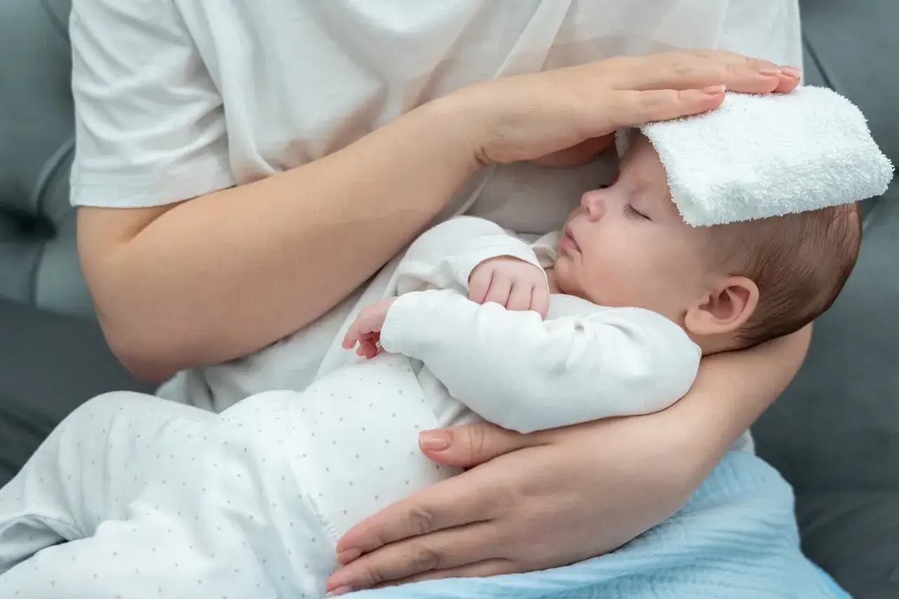 Bebé con paño frío en la frente, cuidando síntomas de covid en bebés.