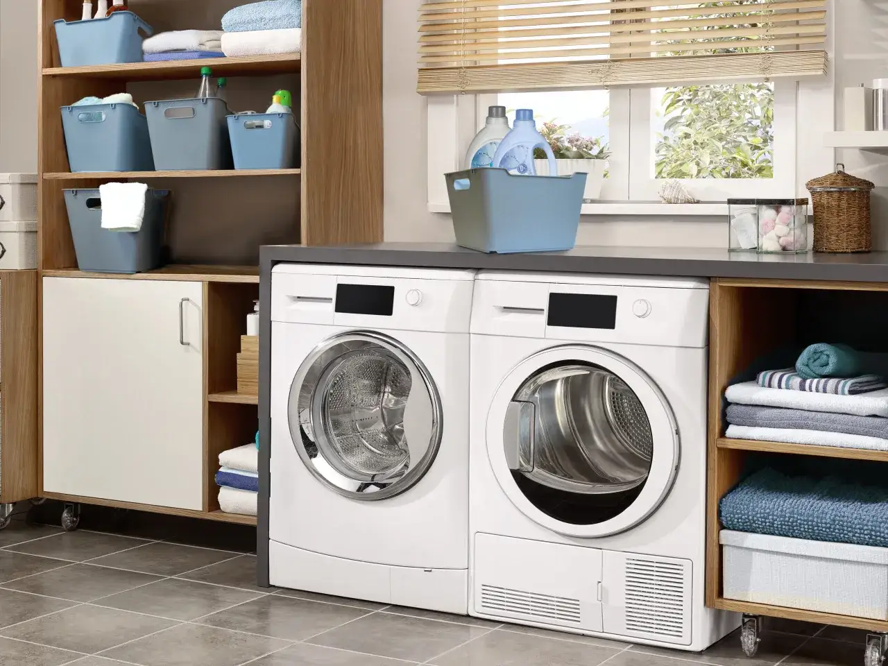 Lavadora y secadora blancas junto a estanter&iacute;as con cestas y toallas. Ideal para lavar ropa a 60 grados y mantener todo ordenado.