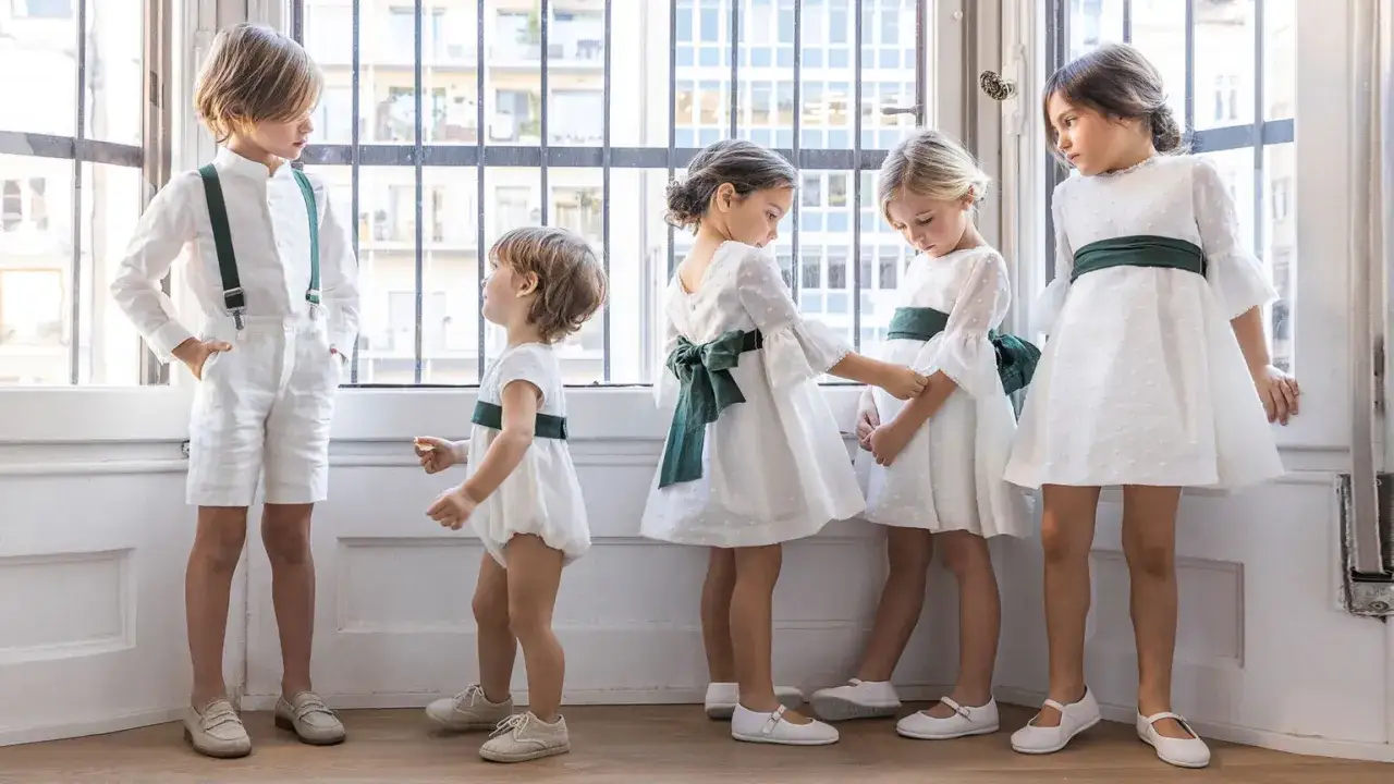 Cinco hermanos de comuni&oacute;n, vestidos de blanco y verde, posan cerca de una ventana.