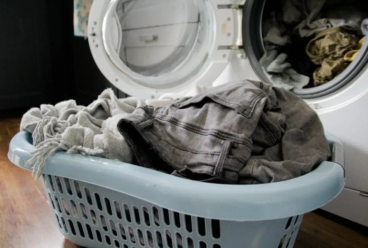 Cesta azul con ropa gris lista para lavar. Aprende como lavar ropa blanca y mantenerla impecable.