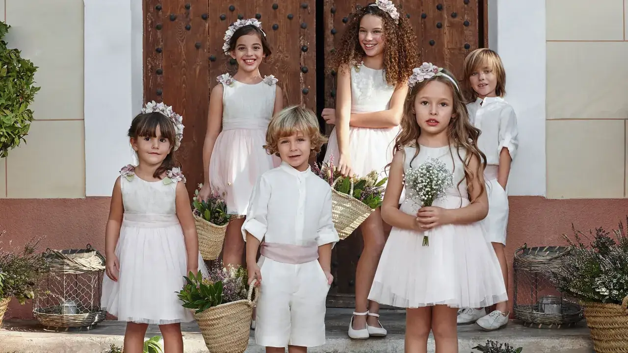 Ni&ntilde;os vestidos de comuni&oacute;n, listos para llevar anillos boda. Flores y cestas adornan la escena.
