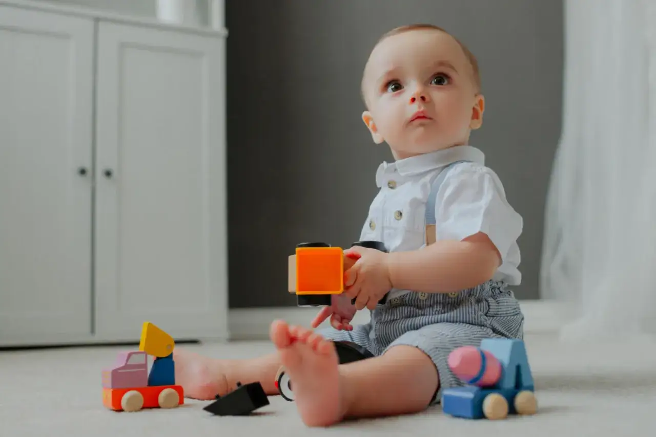Un beb&eacute; sentado en el suelo juega con trenes de madera. Es un momento tierno cuando se sienta un beb&eacute;.