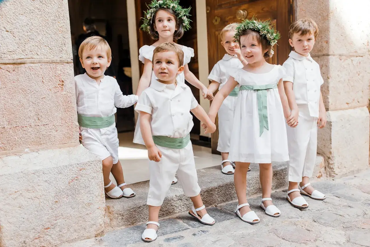 Ni&ntilde;os con trajes blancos y cinturones verdes, como llevan los ni&ntilde;os en una boda, con coronas de flores.