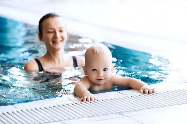 Un bebé sonriente disfruta de la natación con su madre en una piscina.