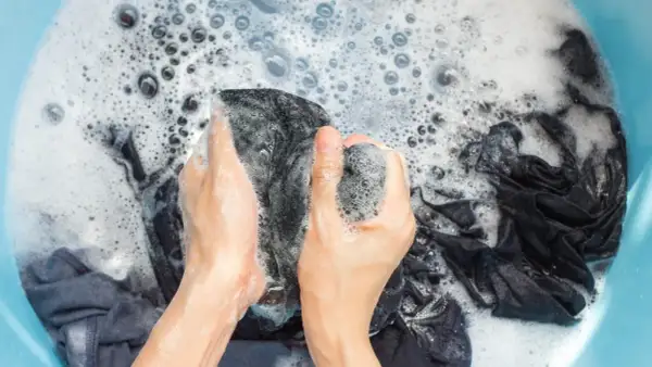 Manos lavando ropa oscura en una tina con espuma. Se puede lavar la ropa con gel de baño para una limpieza suave.